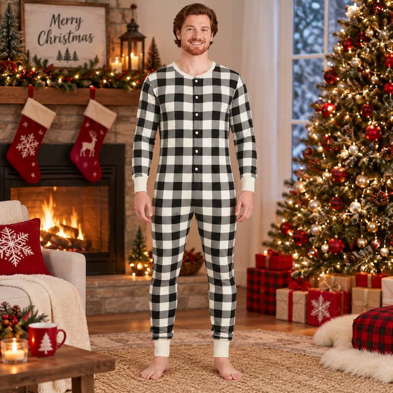 A man wearing a black and white buffalo plaid long-sleeve pajama set stands barefoot in a cozy, decorated Christmas living room with a fireplace, stockings, and a lit Christmas tree.