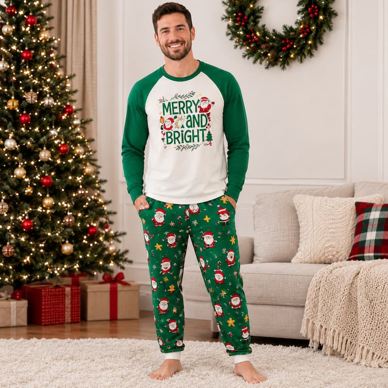 A man wearing a Christmas-themed pajama set stands in a living room. The set includes a white and green raglan long-sleeve shirt with a 'Merry and Bright' Santa graphic, and green pants with a Santa Claus and star pattern.