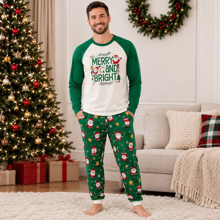 A man wearing a Christmas-themed pajama set stands in a living room. The set includes a white and green raglan long-sleeve shirt with a 'Merry and Bright' Santa graphic, and green pants with a Santa Claus and star pattern.