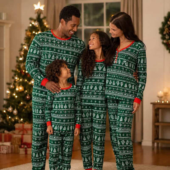 A family of four wearing matching green and white Christmas-themed patterned pajamas, standing together in a cozy living room with a lit Christmas tree in the background.