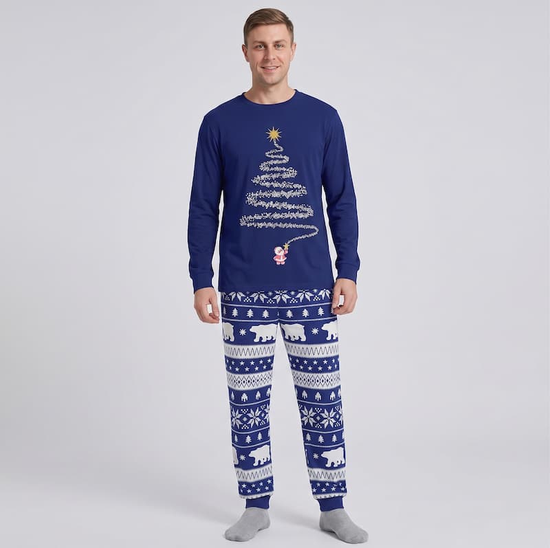 A man modeling a navy blue long-sleeve Christmas pajama set with a white tree graphic and a white Nordic pattern on the pants, set against a light gray studio background.