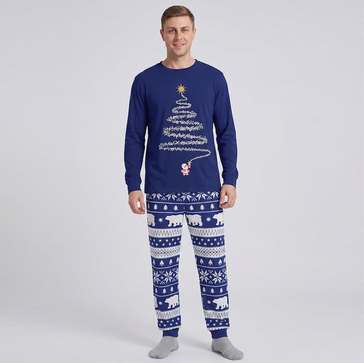 A man modeling a navy blue long-sleeve Christmas pajama set with a white tree graphic and a white Nordic pattern on the pants, set against a light gray studio background.